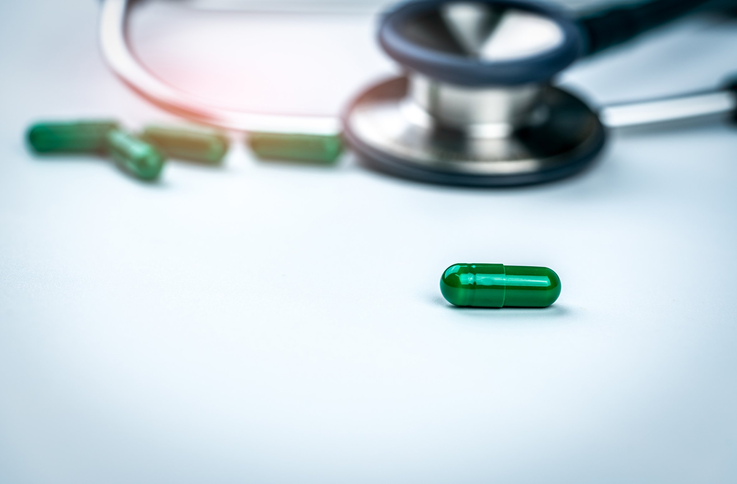 Selective Focus on Green Capsule Pills on Blurred Stethoscope